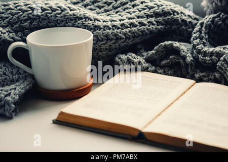 Wollschal, Tasse Tee und Buch auf der Fensterbank. Hygge und gemütliche Herbst Konzept Stockfoto