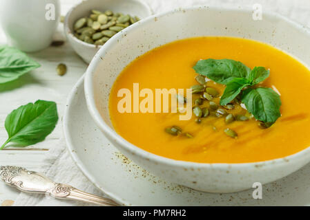 Ernährung Vegetarische Kürbis creme Suppe pürieren, mit Olivenöl, Samen und Basilikum auf einem hölzernen Tisch in eine weiße Platte. Selektiver Fokus Stockfoto