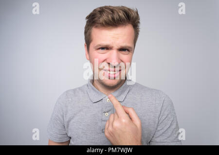 Empörte junge männliche Punkte an sich selbst isoliert über Weiß konkreten Hintergrund. Stockfoto