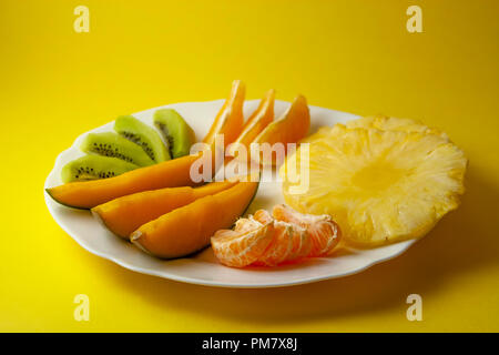 Tropische Früchte, Kiwi, Mango, Ananas, Orange und Mandarine Orange Slices auf weiße Platte auf gelben Hintergrund. Stockfoto