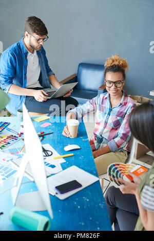 Hohen winkel Porträt des zeitgenössischen afroamerikanischen Frau Brille im Gespräch mit Kollegen am Schreibtisch im Büro Stockfoto