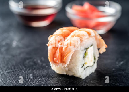 Sushi Rollen frische Garnelen Reis und Philadelphia Käse asiatische Lebensmittel auf dunklem Hintergrund mit eingelegten fermentiert Ingwer Meerrettich Wasabi in Soße Boot Stockfoto