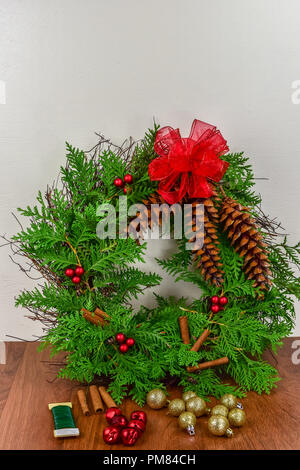 Weihnachten ein Kranz mit Zeder Äste, Tannenzapfen, Zimtstangen, rote Beere Cluster mit einem roten Bogen oben und gold Ornamente, rote Glocken, und Stockfoto