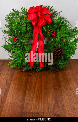 Weihnachten ein Kranz mit Zeder Äste, Tannenzapfen und rote Beere Cluster mit einem roten Bogen auf der Oberseite Stockfoto