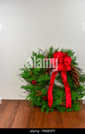 Weihnachten ein Kranz mit Zeder Äste, Tannenzapfen und rote Beere Cluster mit einem roten Bogen auf der Oberseite Stockfoto