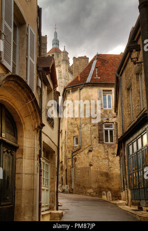 Gasse in der schönen alten französischen Stadt Dole, der Turm der Kirche von Notre-Dame und dunkle Wolken über dem alten Häuser Stockfoto