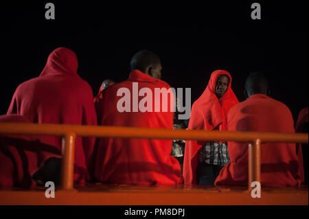 Migranten mit roten Decken, die aus einem beiboot im Mittelmeer gerettet wurden, gesehen werden, die in ein Rettungsboot nach ihrer Ankunft am Hafen von Malaga in einer regnerischen Nacht aussteigen. Mitglieder der Spanischen Sicherheit auf See gerettet Insgesamt 161 Migranten an Bord verschiedenen Jollen vom Mittelmeer und brachte sie nach Malaga Hafen, wo sie durch das Spanische Rote Kreuz unterstützt wurden. Stockfoto