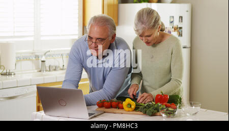 Senior Paar mit Laptop Rezepte Schneiden von Gemüse in der Küche Stockfoto