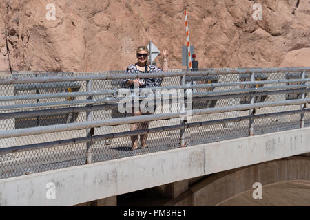 Weibliche Wanderer Besucher der Hoover Dam lächelt und macht ein friedenszeichen Geste, während auf der Brücke zu Fuß über den Hoover Dam Stockfoto