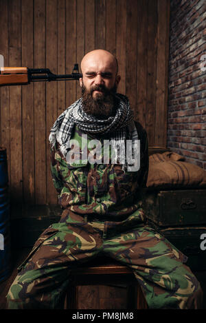 Captive Soldat sitzt auf einem Stuhl gebunden, Pistole zeigte auf seinen Kopf, den Schrecken des Krieges. Terrorismus und Terror, militärischen Mann in khaki Camouflage auf interrogati Stockfoto