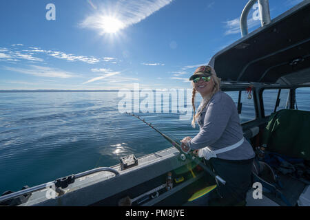 Blonde Frau Fischer Fischen für Heilbutt in den Cook Inlet von Alaska auf einem Fischerboot. Rod und Reel in der Hand Stockfoto
