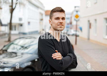 Stilvolle junger Mann in einem schwarzen T-Shirt in der Nähe des Auto Stockfoto