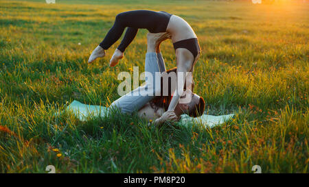 Familie Paar Üben Yoga auf dem Gras bei Sonnenuntergang. Gesunder Lebensstil Stockfoto