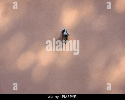 Single shiny Brass Lantern wirft Schatten auf ansonsten Einfache texturierte Wand mit Pools von dappled Licht in Seix in der Ariège Pyrenäen, Frankreich Stockfoto
