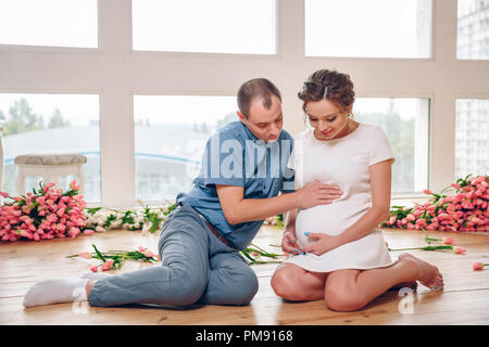 Gerne schwangere Frau mit ihrem Mann halten und hören auf Baby im Bauch und Einstellung auf den Fußboden zu Hause, Schwangere und Familie Konze Stockfoto