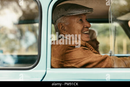 Seitenansicht der lächelnden alten Mann mit Hut fährt einen Oldtimer mit Frau an der Rückseite sitzen. Senior Paar gehen auf Fahrt. Stockfoto
