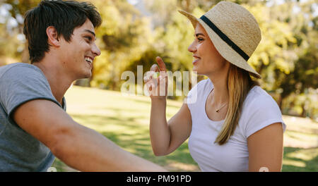 Lächelndes Paar an jedem anderen sitzen in einem Park. Frau mit Hut sitzt mit ihrem Freund eine Traube. Stockfoto
