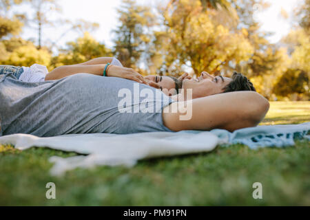 Paar entspannende in einem Park liegen auf dem Boden und Reden. Frau schlafen auf Arm von ihrem Freund in einem Park an einem sonnigen Tag. Stockfoto