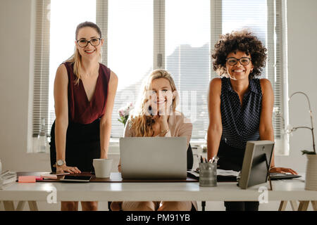 Portrait von lächelnden Jungen geschäftsfrau am Schreibtisch und lächelnd an der Kamera. Multirassischen Geschäftsfrauen im Amt. Stockfoto