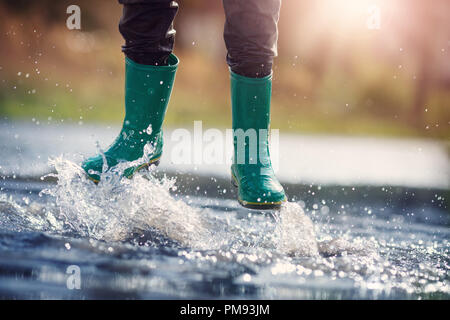 Kind zu Fuß in Gummistiefel in Pfütze auf Regenwetter Stockfoto