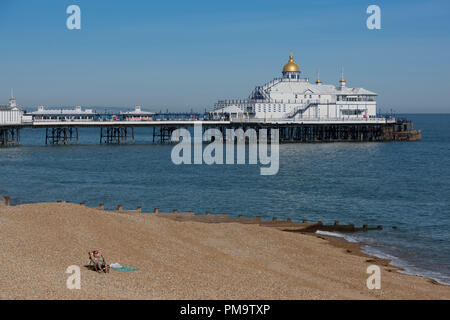 Ein einsamer Sonnenanbeter am Strand von Brighton in der Grafschaft East Sussex an der Südküste von England mit der Pier hinter sich. Stockfoto