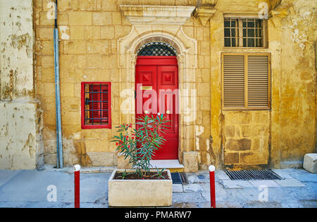 Die alte steinerne Gebäude dekoriert mit Holzmöbeln hell rote Tür mit relief Türrahmen, die hl. Ursula Street, Valletta, Malta. Stockfoto