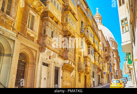 VALLETTA, MALTA - 17. Juni 2018: Das hügelige Alte Münze Straße mit hohen Wohn- bauten und einen Blick auf die riesige Kuppel der Karmeliterkirche, am 17. Juni in V Stockfoto