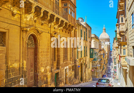 VALLETTA, MALTA - 17. JUNI 2018: Zu Fuß die engen Alte Münze Straße mit Abfahrten und Anstiege und ein Blick auf die riesige Kuppel der Karmeliterkirche und historischen Stockfoto