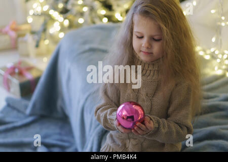 Kleines Mädchen hält Glas Kugel in den Händen. Spielzeug für die Dekoration Weihnachtsbaum. Glückliche Kindheit. Stockfoto