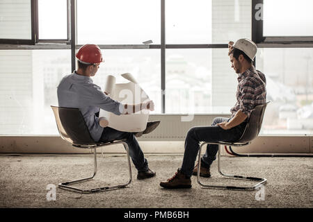 Ingenieur ist das Öffnen der Blaupause während sein Partner setzen auf ein Schutzhelm ist Stockfoto