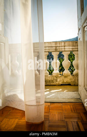 Fließende Gardinen wehen im Wind, als sie zu der alten Europäischen hotel Balkon mit Blick schaffen eine romantische Atmosphäre in Opatija, Kroatien führen. Stockfoto