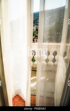 Fließende Gardinen wehen im Wind, als sie zu der alten Europäischen hotel Balkon mit Blick schaffen eine romantische Atmosphäre in Opatija, Kroatien führen. Stockfoto