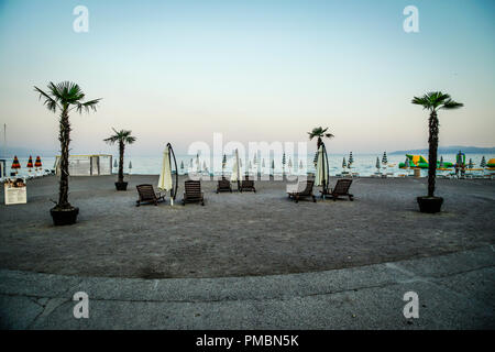 Leere Liegestühle mit großen Heruntergeklappt Sonnenschirme und Palmen säumen die Küste in der Abenddämmerung in Opatija an der Adria in Kroatien Stockfoto