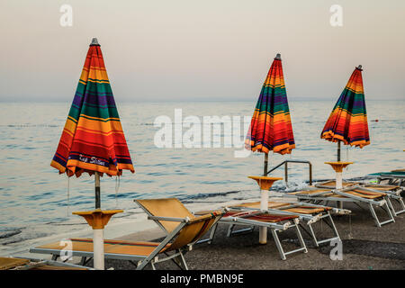 Leere Liegestühle mit großen Heruntergeklappt Sonnenschirme säumen die Uferpromenade am Sonnenuntergang in Opatija an der Adria in Kroatien Stockfoto