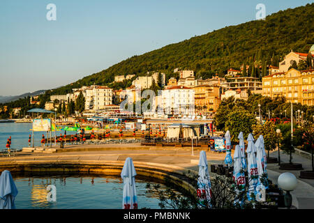 Leere Liegestühle mit großen Heruntergeklappt Sonnenschirme säumen die Uferpromenade am Sonnenuntergang in Opatija an der Adria in Kroatien Stockfoto