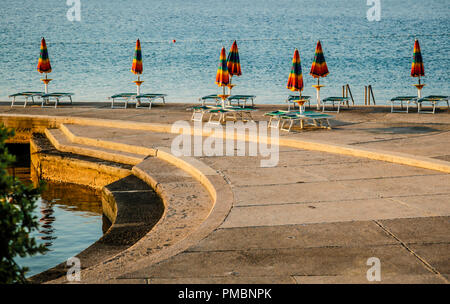 Leere Liegestühle mit großen Heruntergeklappt Sonnenschirme säumen die Uferpromenade am Sonnenuntergang in Opatija an der Adria in Kroatien Stockfoto