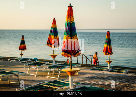 Leere Liegestühle mit großen Heruntergeklappt Sonnenschirme säumen die Uferpromenade am Sonnenuntergang in Opatija an der Adria in Kroatien Stockfoto