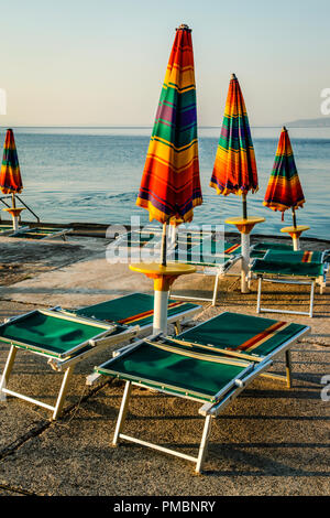 Leere Liegestühle mit großen Heruntergeklappt Sonnenschirme säumen die Uferpromenade am Sonnenuntergang in Opatija an der Adria in Kroatien Stockfoto