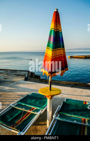 Leere Liegestühle mit großen Heruntergeklappt Sonnenschirme säumen die Uferpromenade am Sonnenuntergang in Opatija an der Adria in Kroatien Stockfoto