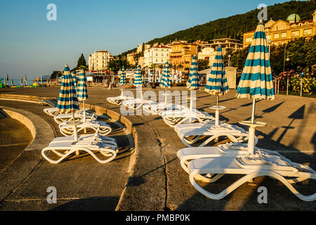 Leere Liegestühle mit großen Heruntergeklappt Sonnenschirme säumen die Uferpromenade am Sonnenuntergang in Opatija an der Adria in Kroatien Stockfoto