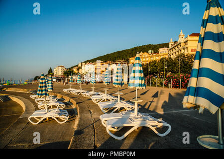 Leere Liegestühle mit großen Heruntergeklappt Sonnenschirme säumen die Uferpromenade am Sonnenuntergang in Opatija an der Adria in Kroatien Stockfoto