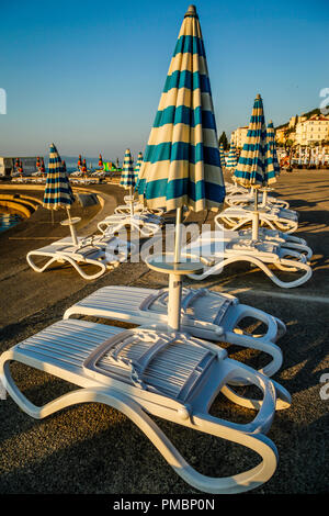 Leere Liegestühle mit großen Heruntergeklappt Sonnenschirme säumen die Uferpromenade am Sonnenuntergang in Opatija an der Adria in Kroatien Stockfoto