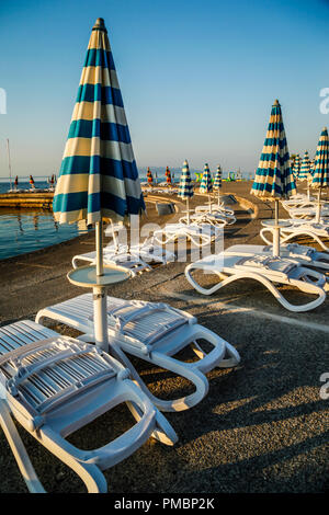 Leere Liegestühle mit großen Heruntergeklappt Sonnenschirme säumen die Uferpromenade am Sonnenuntergang in Opatija an der Adria in Kroatien Stockfoto