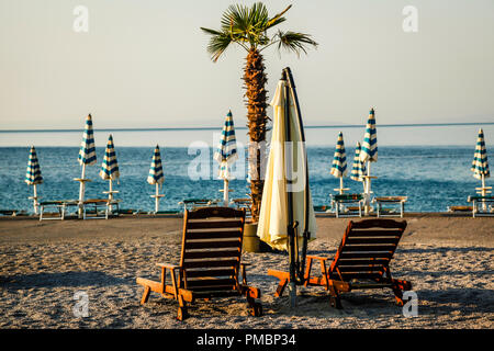 Leere Liegestühle mit großen Heruntergeklappt Sonnenschirme säumen die Uferpromenade am Sonnenuntergang in Opatija an der Adria in Kroatien Stockfoto