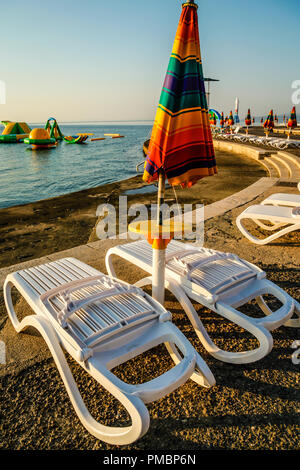 Leere Liegestühle mit großen Heruntergeklappt Sonnenschirme säumen die Uferpromenade am Sonnenuntergang in Opatija an der Adria in Kroatien Stockfoto