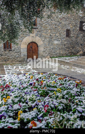 Schönen Straße von Andorra la Vella Stadt durch plötzliche Schnee gefangen. Blühen bunte Leben Blumen unter Schneedecke im Vordergrund. Allgemeinen Rat und Stockfoto