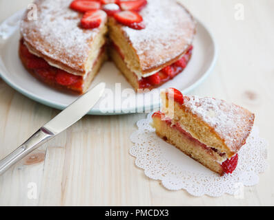 Victoria Schwamm Kuchen mit Erdbeeren, Marmelade und Sahne mit ein ausgeschnittenes Stück auf einem Holztisch Stockfoto