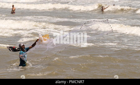 Goa, Indien - 29. Mai 2017: Ein unbekannter einheimischer Fischer wirft einen Net im flachen Meer, während Touristen auf, am 29. Mai 2017, in Goa, Indien Stockfoto