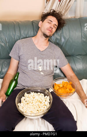 Ein Mann schlafen auf einer Couch in einem Durcheinander von Junk Food Stockfoto