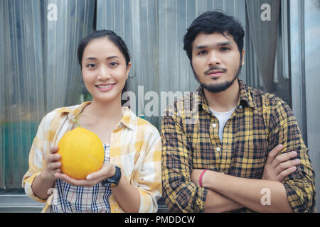 Zwei Bauern stehen mit einer Melone und Lächeln auf der Farm gerne Stockfoto